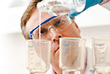 Scientist wearing safety glasses pouring a clear liquid from a bottle into a laboratory beaker