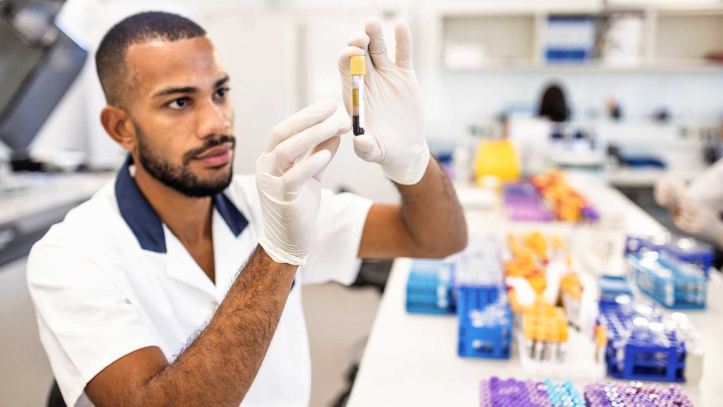 A lab technician examines a vial of liquid of blood.