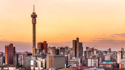 sunset view of Johannesburg South Africa city skyline featuring tall buildings, a prominent tower, and clear blue sky.