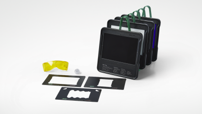 Scientific imaging kit. Five upright black trays with green handles stand on the right. Three flat black alignment guides, yellow safety glasses, and a small lens sit in the foreground.