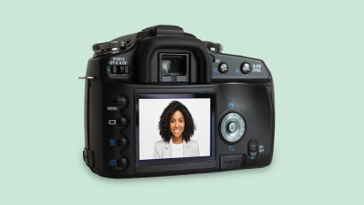 Back of a DSLR camera on a pale green background. The LCD screen displays a portrait of a smiling person.